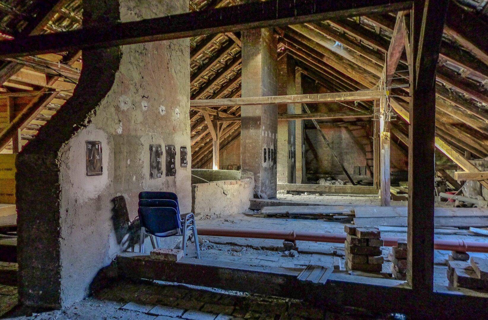 Großer Dachbodenbereich mit freiliegenden Holzbalken, Ziegelwänden und alten Möbeln.