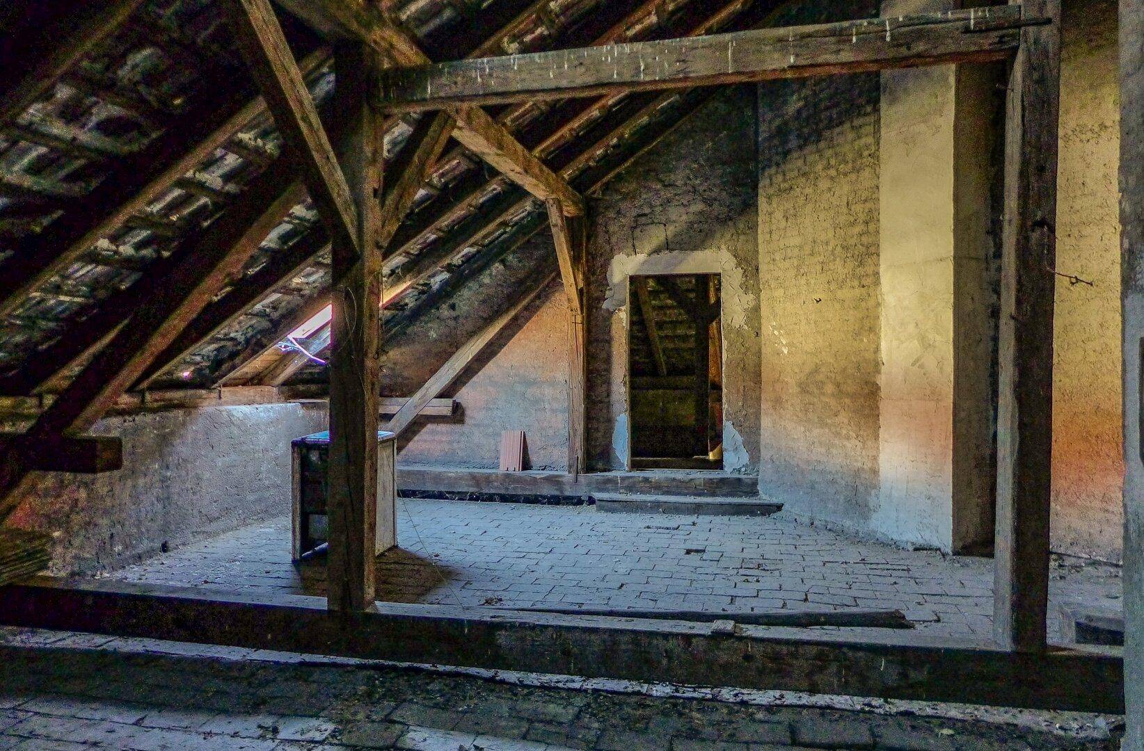 Dachboden mit sichtbarer Holzkonstruktion, Ziegelboden und einem Durchgang zu weiteren Bereichen.