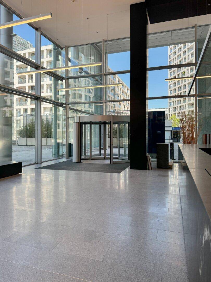 Helle und moderne Lobby mit großen Glasfronten, Drehkreuz und hellem Fliesenboden.