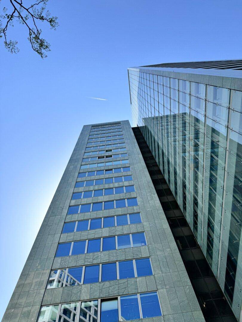 Hohes Gebäude mit blauen Glasfenstern und grauer Fassade, das in den klaren blauen Himmel ragt.