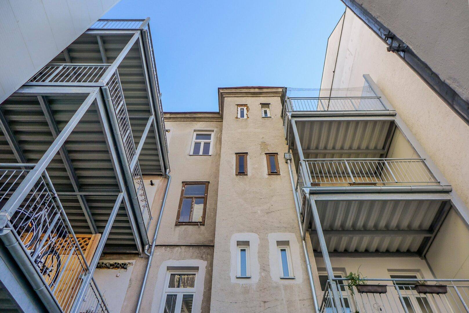 Rückfassade eines Altbaus mit mehreren externen Metallbalkonen und Fenstern.