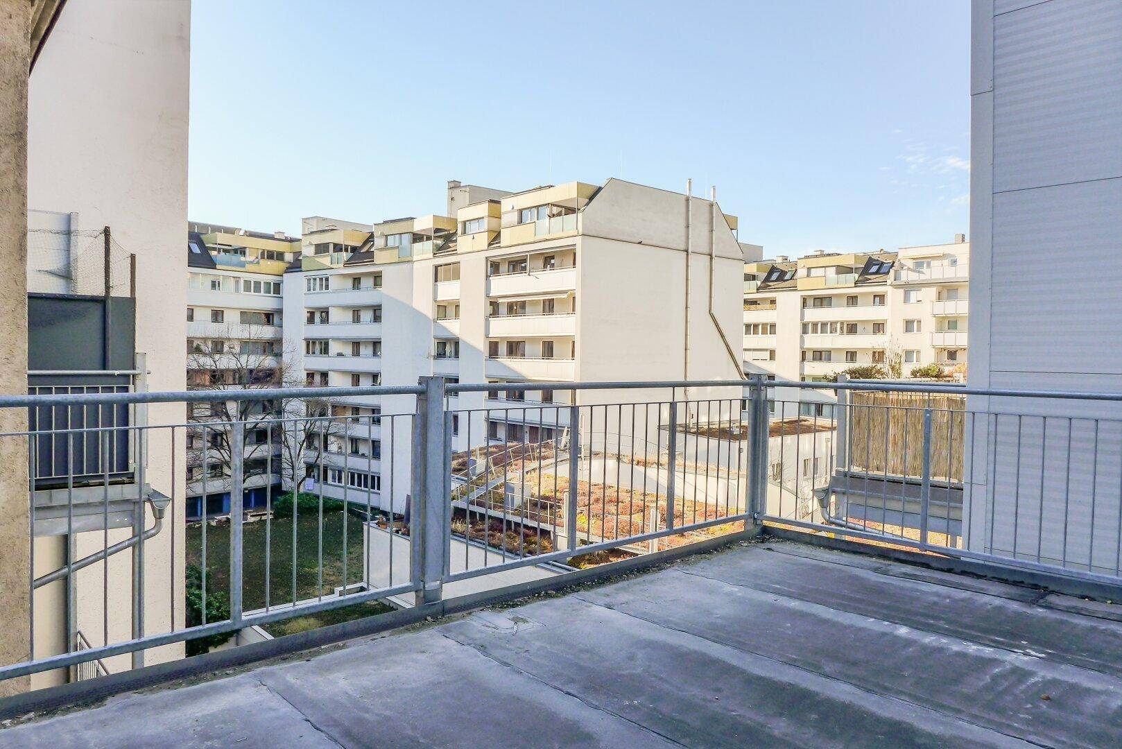 Große, unmöblierte Dachterrasse mit Blick auf den Innenhof und umliegende Wohngebäude.