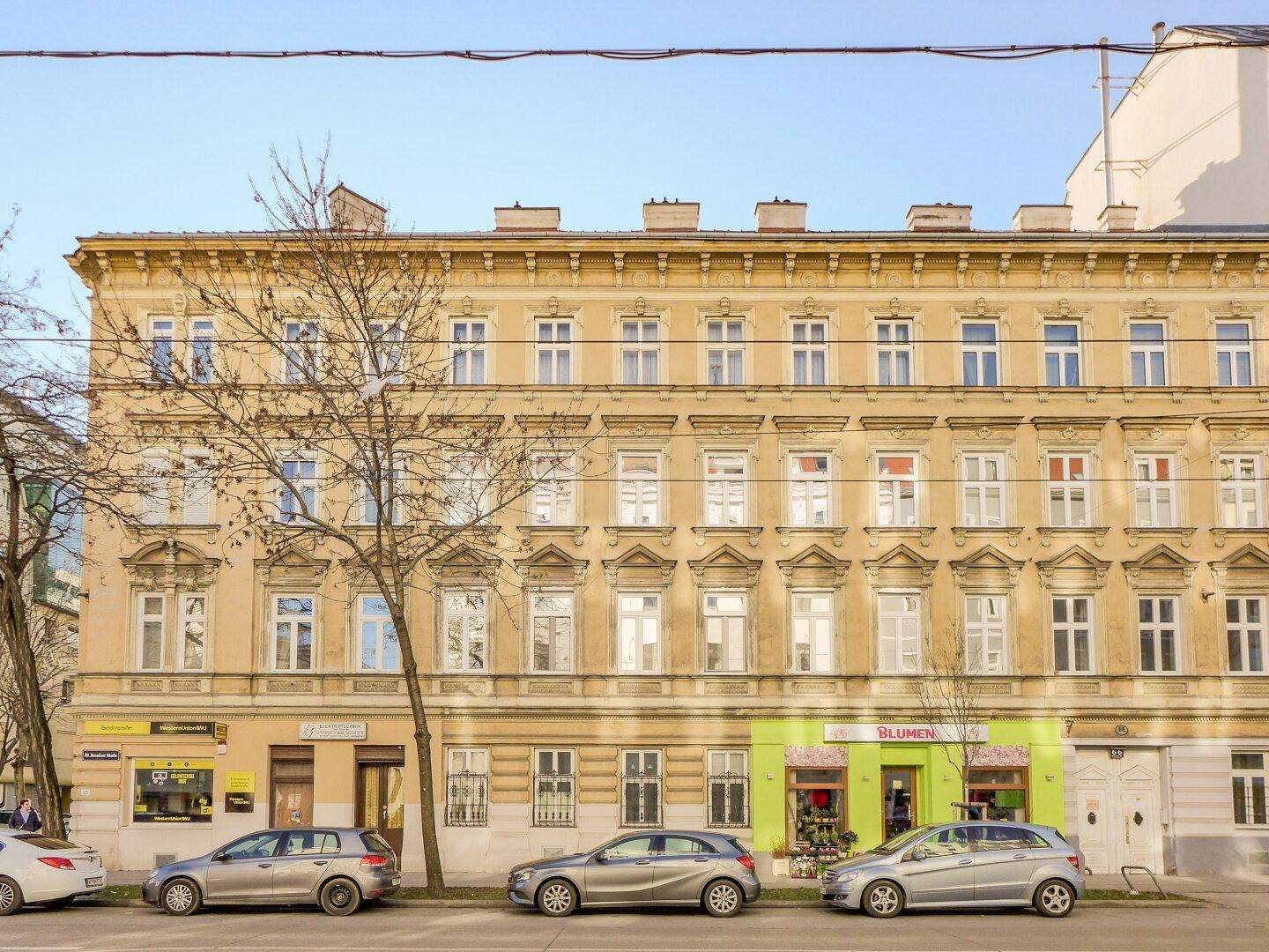 Historisches Mehrfamilienhaus mit klassischer Fassade, vielen Fenstern und Geschäften im Erdgeschoss.