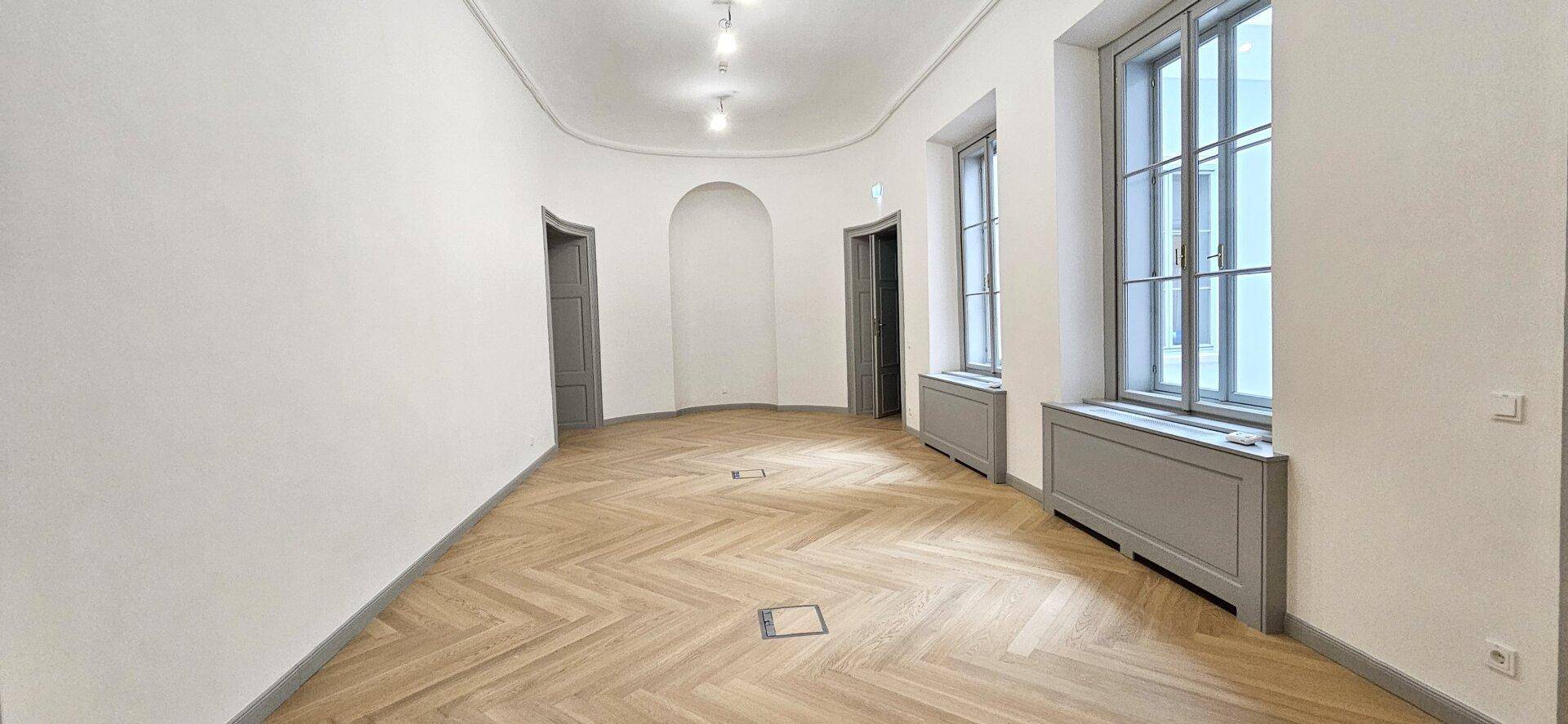 Langer, heller Raum mit Fischgrätparkett, hohen Fenstern und eleganten Rundbögen, schafft eine offene Atmosphäre.