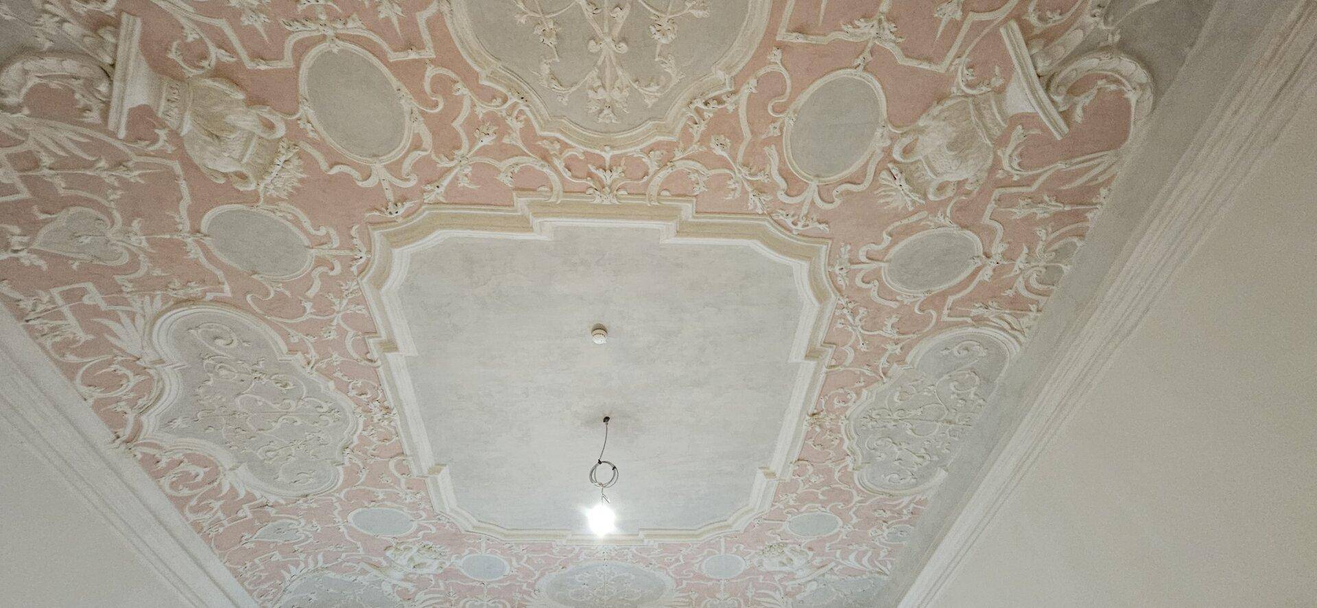 Historische Stuckdecke mit aufwendigen Verzierungen in Rosa und Weiß, ein beeindruckendes Detail.
