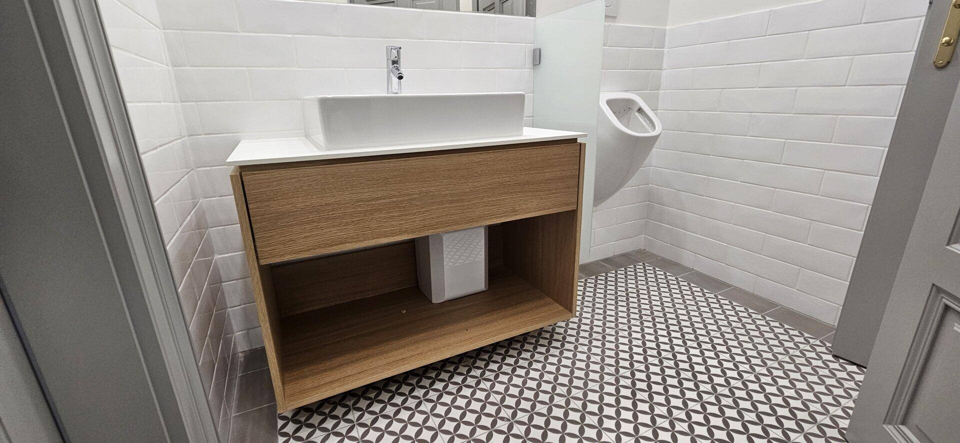 Modernes Badezimmer mit weißem Waschbecken, Holzunterschrank und gemusterten Fliesen, sehr stilvoll.