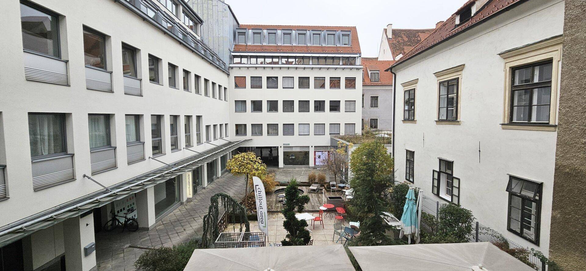 Blick auf einen begrünten Innenhof, umgeben von Gebäuden mit modernen und traditionellen Fassaden, sehr ansprechend.