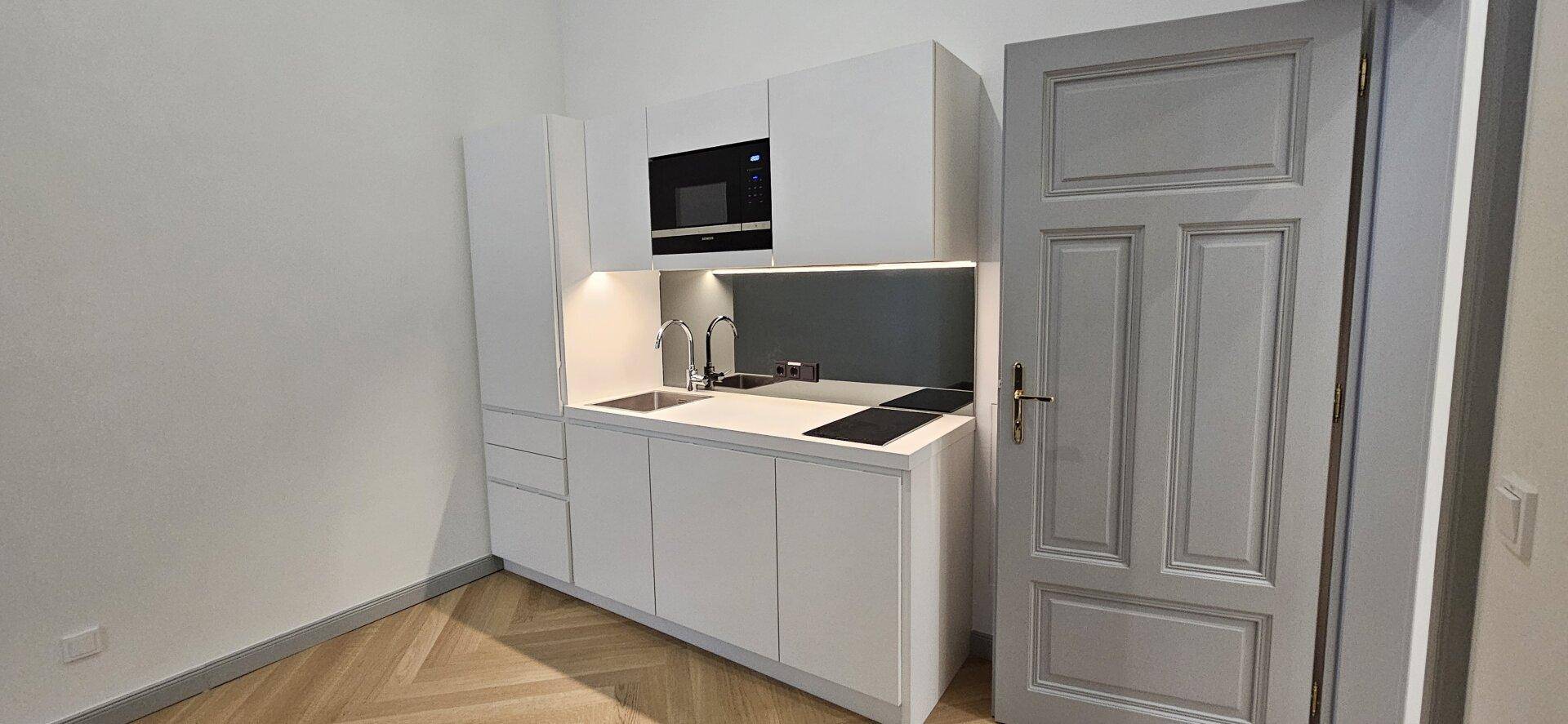 Moderne, kompakte Küchenzeile in Weiß mit integriertem Backofen und Kochfeld, ideal für kleine Räume.