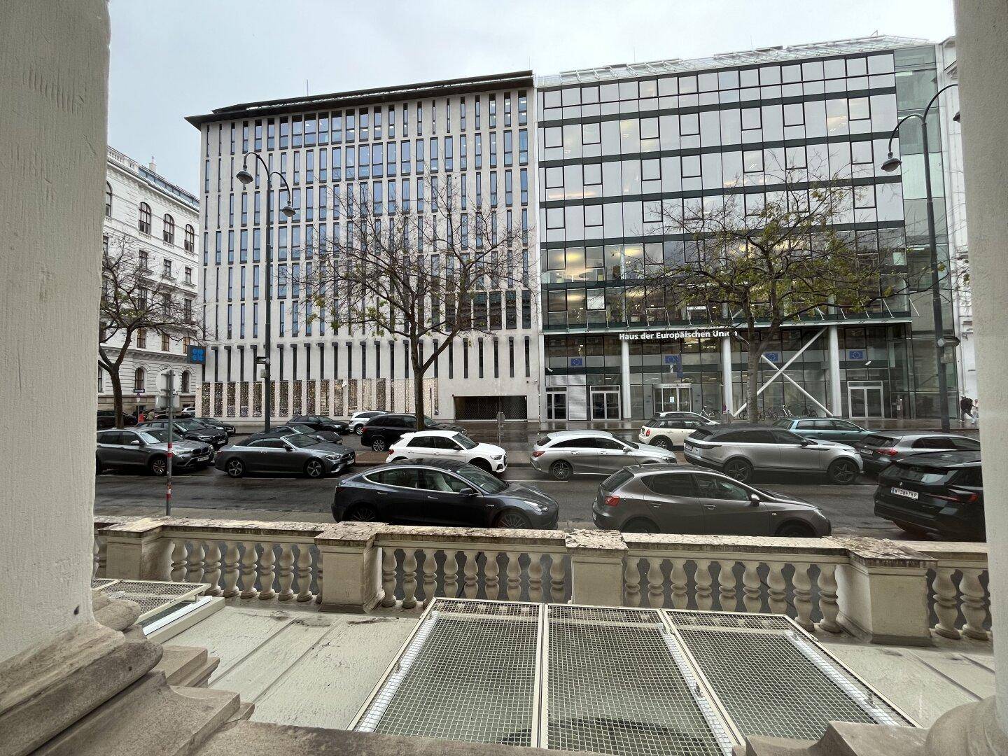 Blick auf eine belebte Straße mit modernen Bürogebäuden und parkenden Autos in der Stadt.