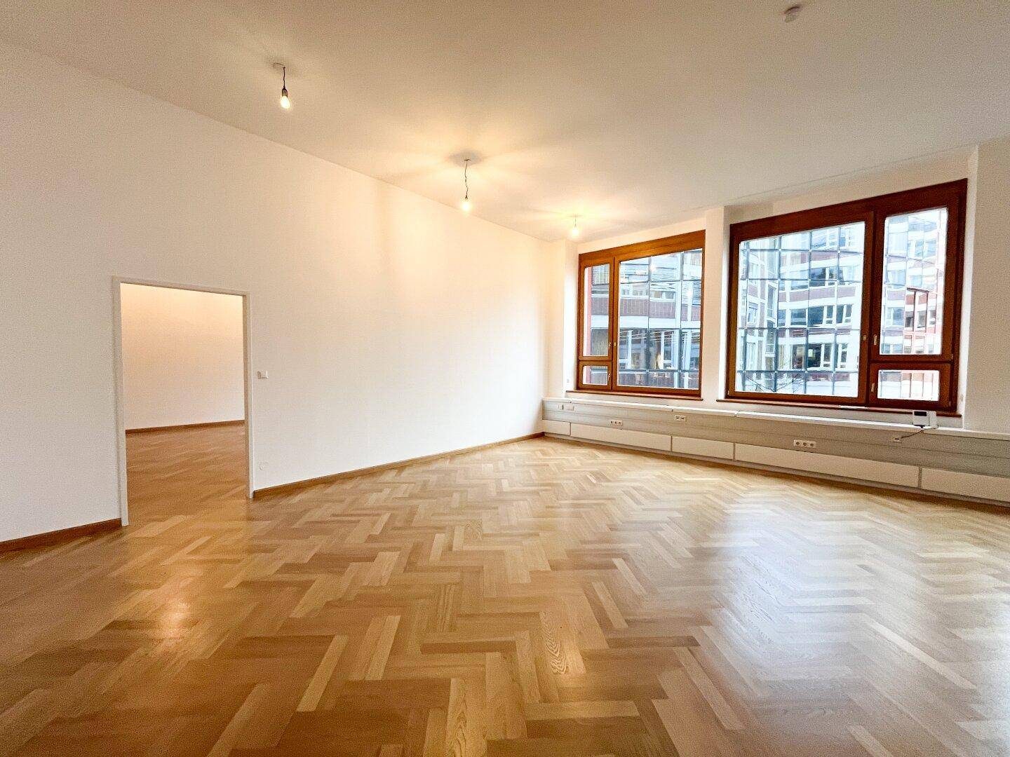 Geräumiger, heller Raum mit Fischgrätparkett und großen Fenstern, die einen Blick auf die Stadt bieten.