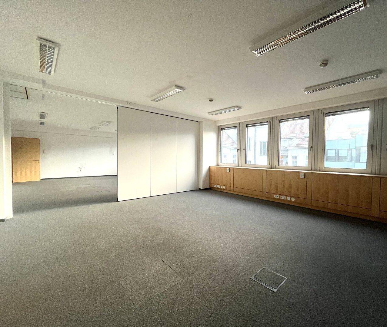 Flexibles Büro mit Teppichboden, großen Fenstern und verschiebbaren Trennwänden für individuelle Raumgestaltung.