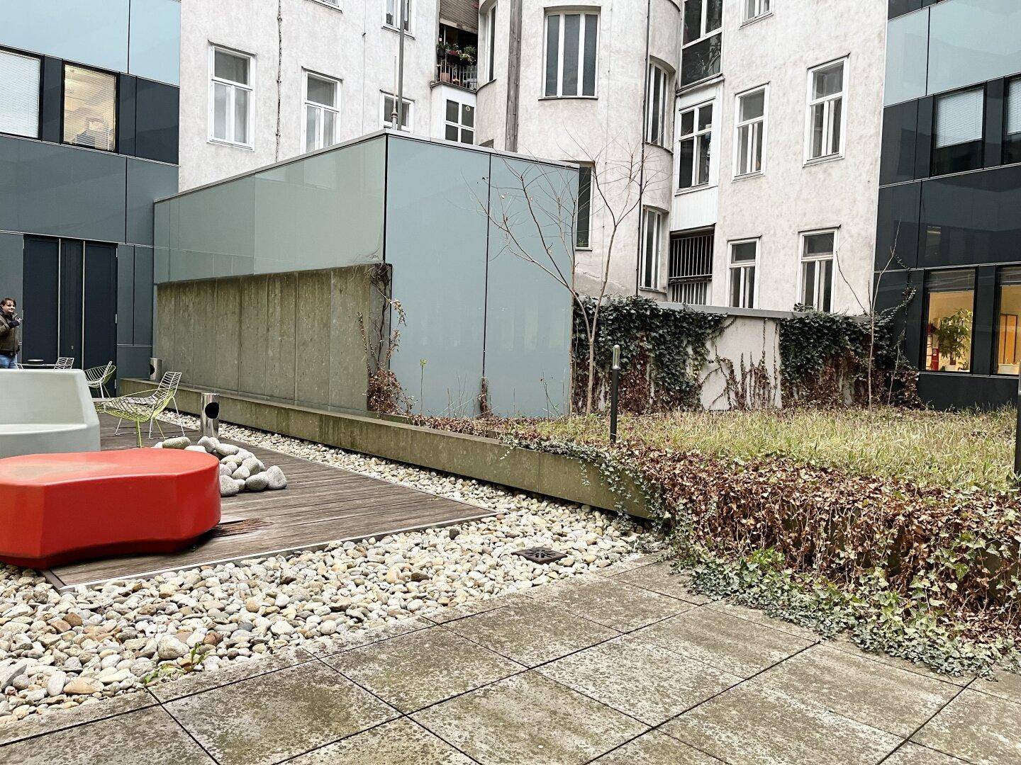 Ruhiger Innenhof mit Holzdeck, Kiesflächen und verschiedenen Pflanzen, ideal zum Entspannen.