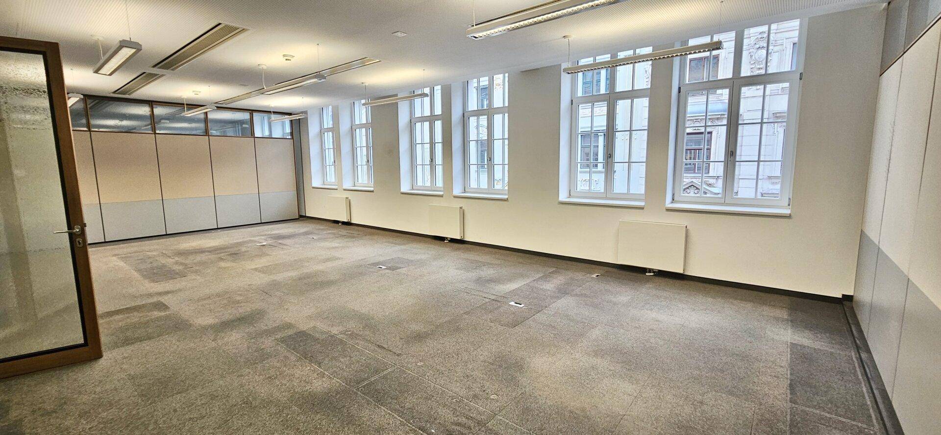 Helles Büro mit vielen Fenstern, Teppichboden und schlichten weißen Wänden, bereit zur Einrichtung.