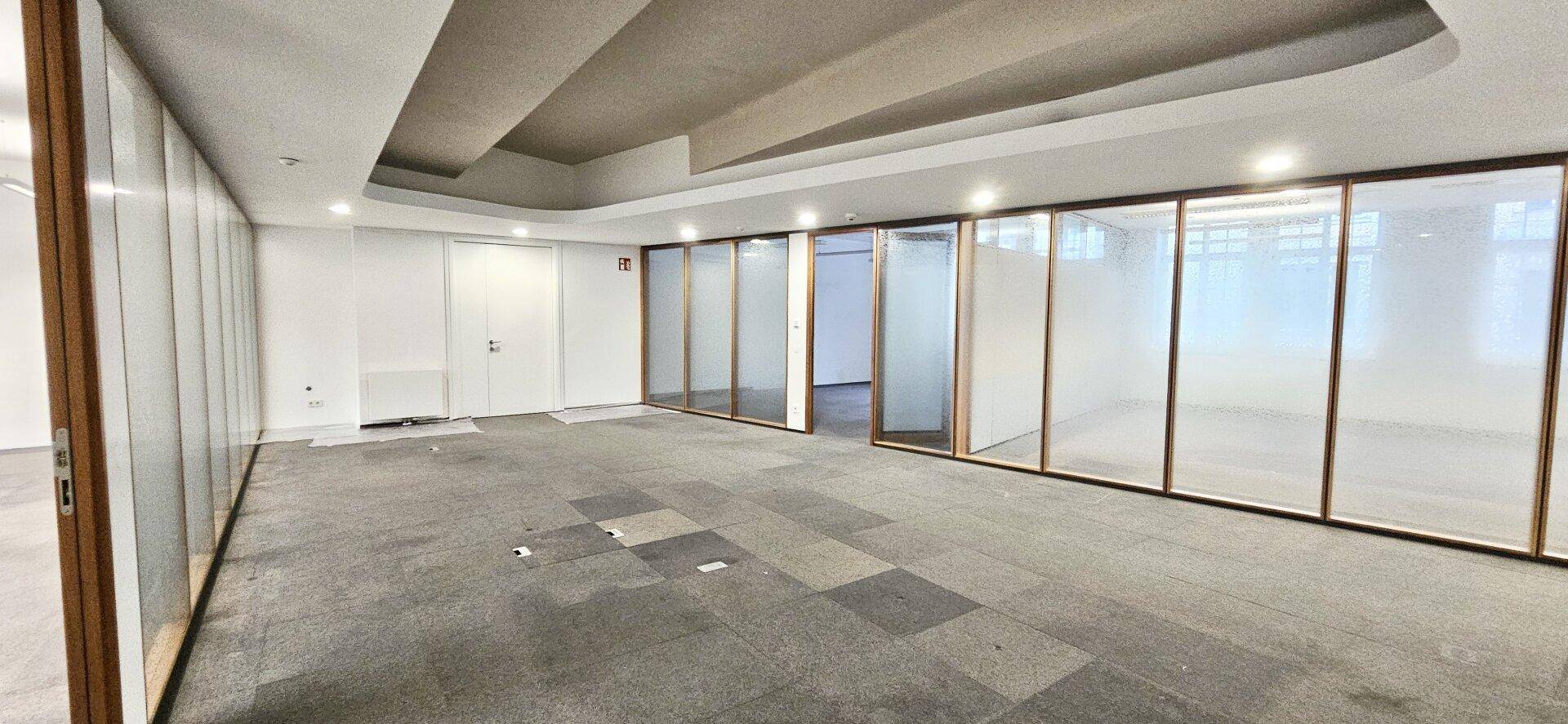 Geräumiges Büro mit Teppichboden und modernen Glasabtrennungen für separate Arbeitsbereiche.