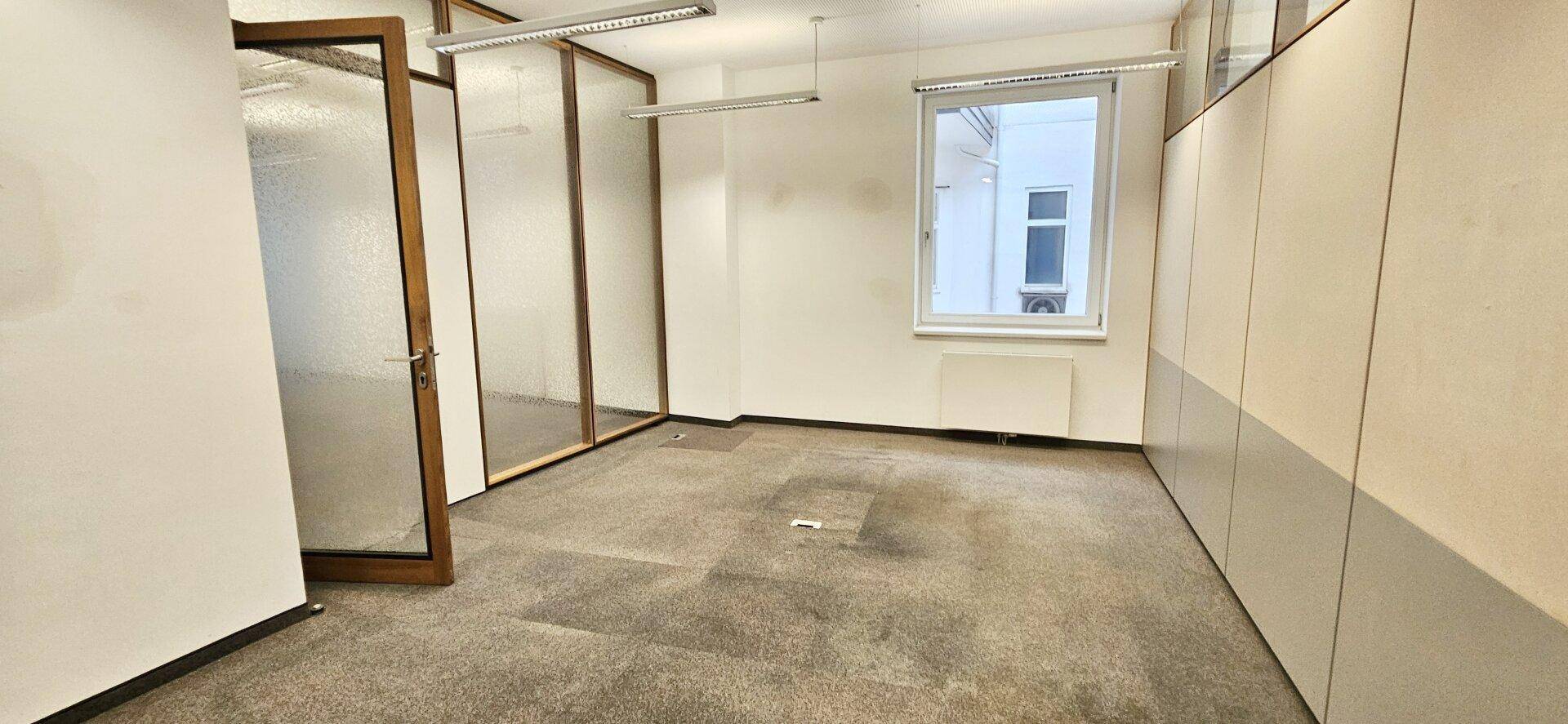Geräumiges Büro mit Teppichboden und einer Fensterfront, die den Raum hell und einladend macht.