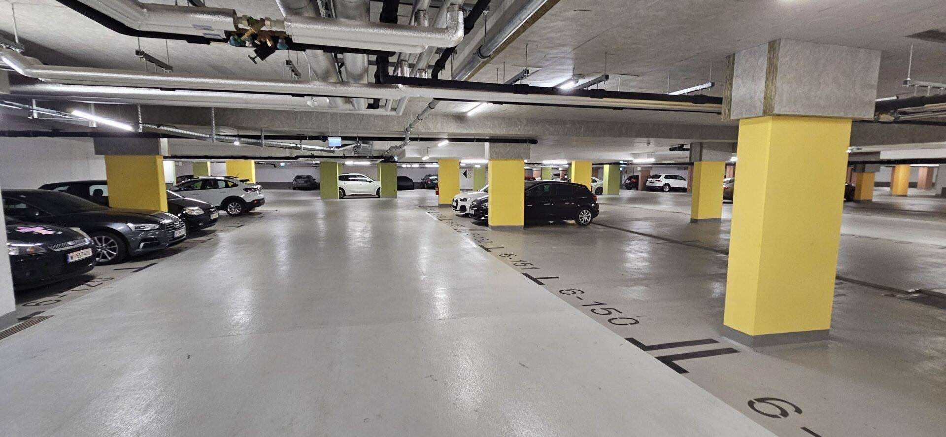 Helle und saubere Tiefgarage mit vielen Parkplätzen und gelben Stützpfeilern.