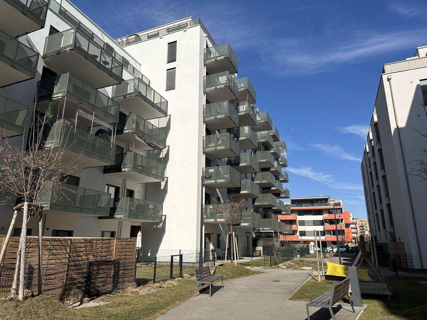 Moderne Wohngebäude mit zahlreichen Balkonen, Glasbrüstungen und gepflegten Grünflächen.