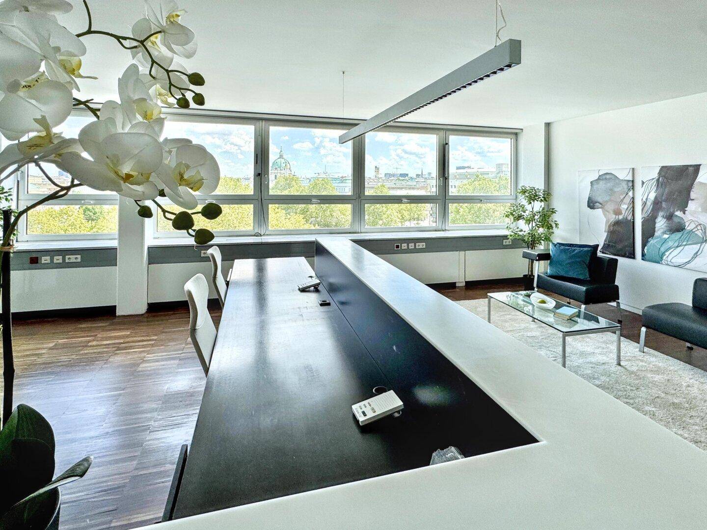 Moderner Büroraum mit langem Konferenztisch, Holzboden und Blick auf die Stadt durch große Fenster.