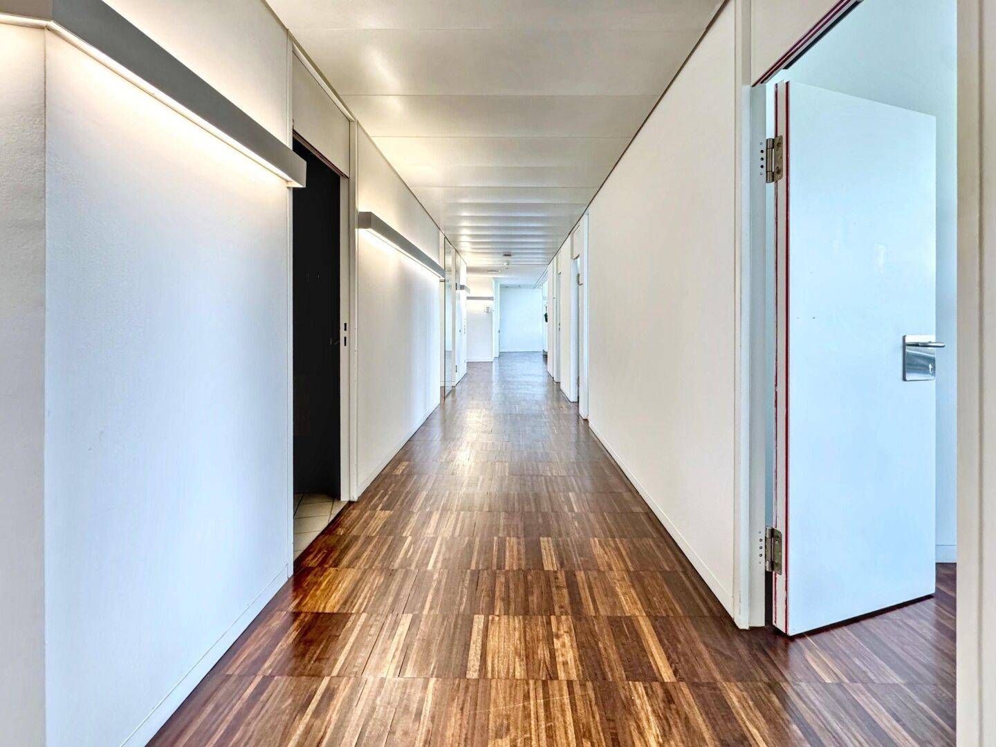 Langer, heller Flur mit Holzboden und mehreren Türen, der verschiedene Büroräume verbindet.
