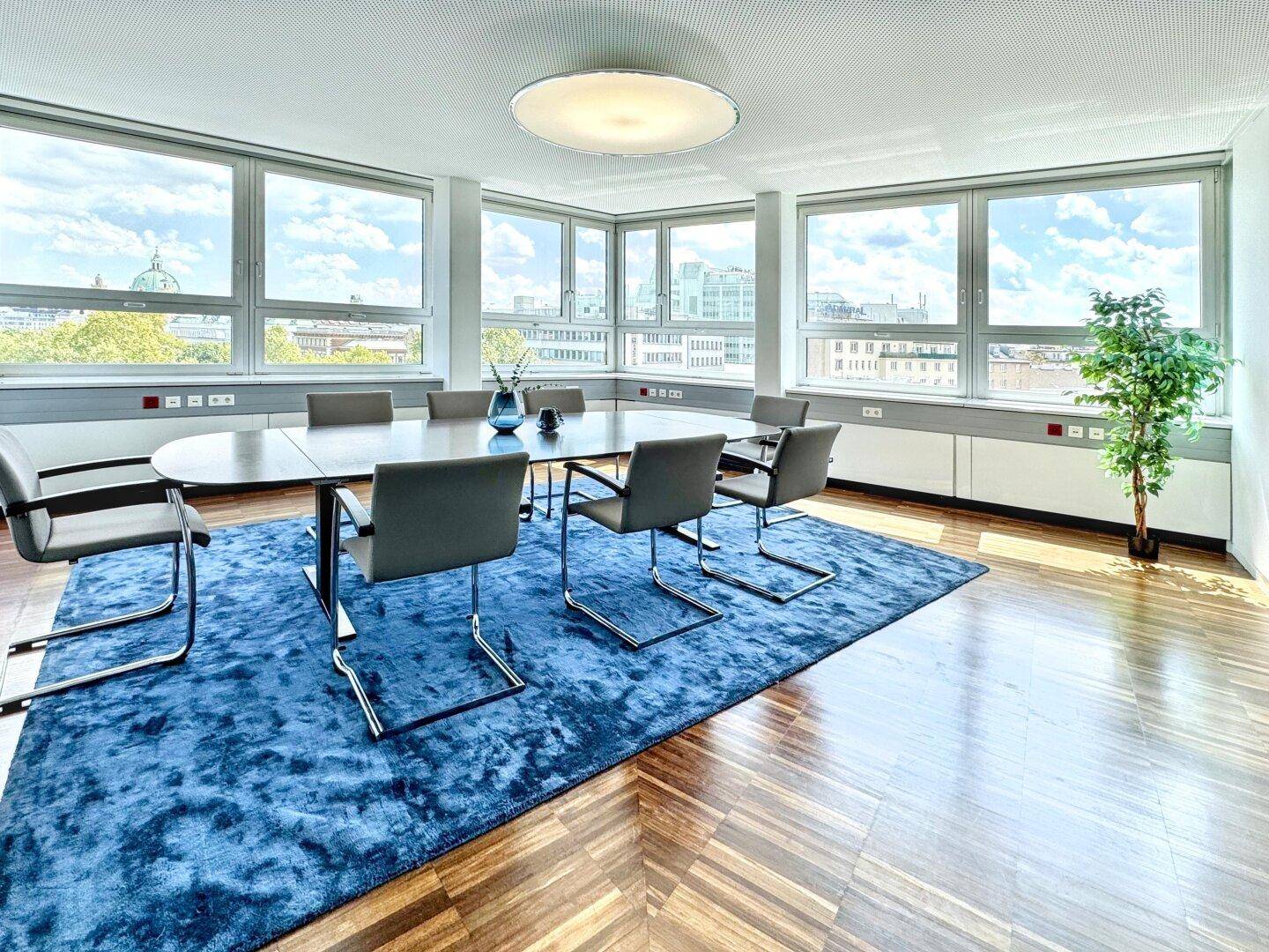 Heller Konferenzraum mit ovalem Tisch, bequemen Stühlen und Panoramablick auf die Stadt.