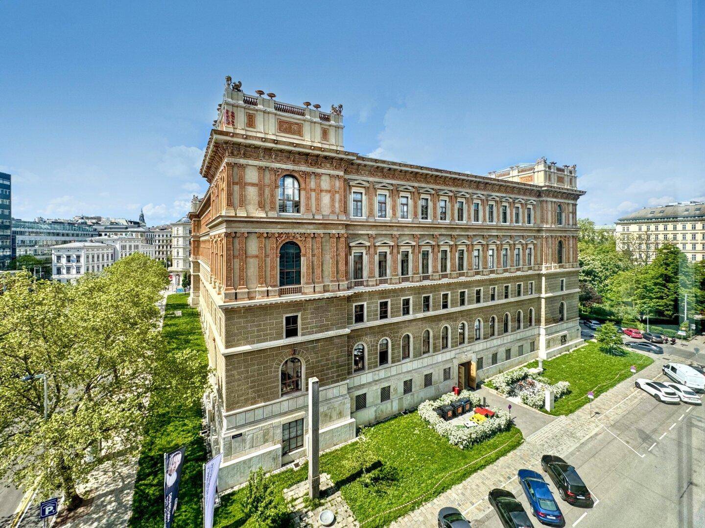 Historisches Gebäude mit beeindruckender Architektur, umgeben von Grünflächen und einer Straße.