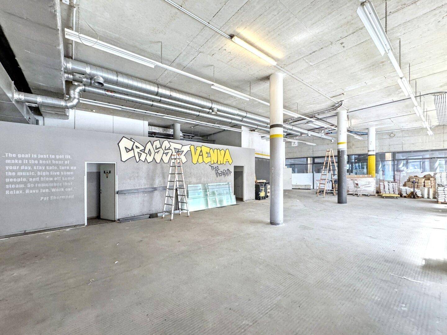 Weitläufiger Gewerberaum mit Betonwänden, hohen Decken und urbaner Wandgestaltung.
