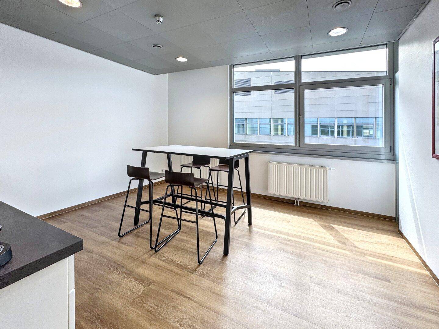 Kleinerer Bürobereich mit Holzboden, Stehtisch und Hockern, ideal für kurze Pausen oder Besprechungen.