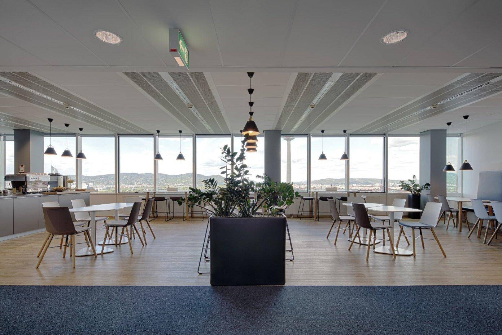 Helle Cafeteria mit vielen Tischen, Stühlen und Panoramablick auf die umliegende Landschaft.