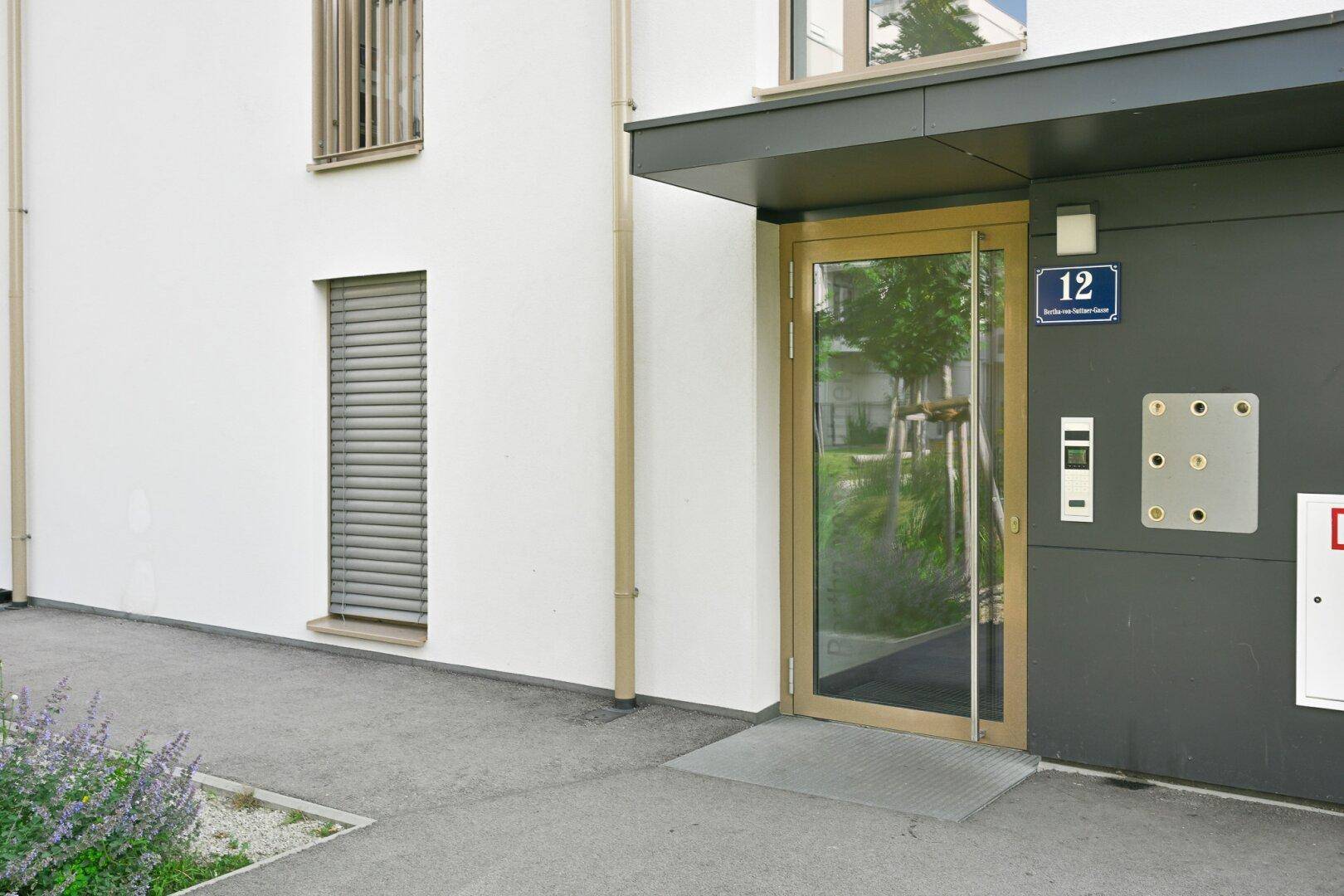 Moderner Eingangsbereich eines Wohngebäudes mit Glasfassade und Hausnummer 12.