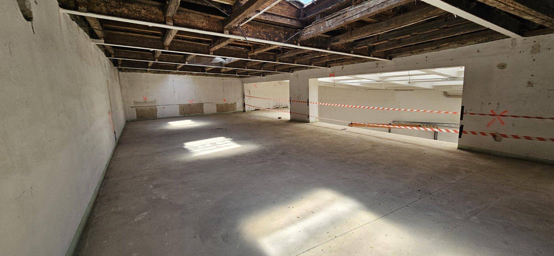 Großer, leerer Raum mit Betonboden und sichtbaren Holzdeckenbalken, der viel Potenzial für Umbau bietet.