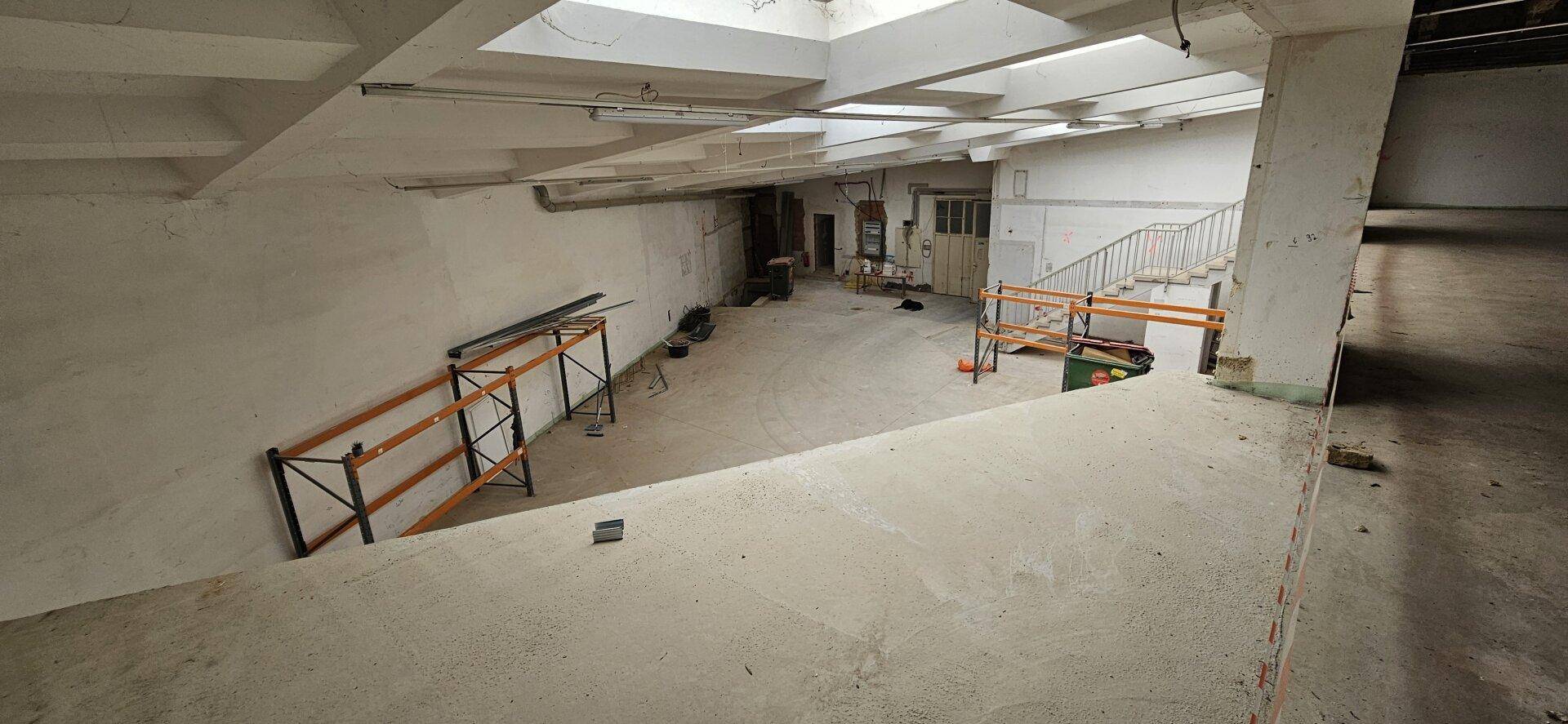 Weitläufiger Industrieraum mit Betonboden, hohen Decken und einer Rampe, die verschiedene Ebenen verbindet.