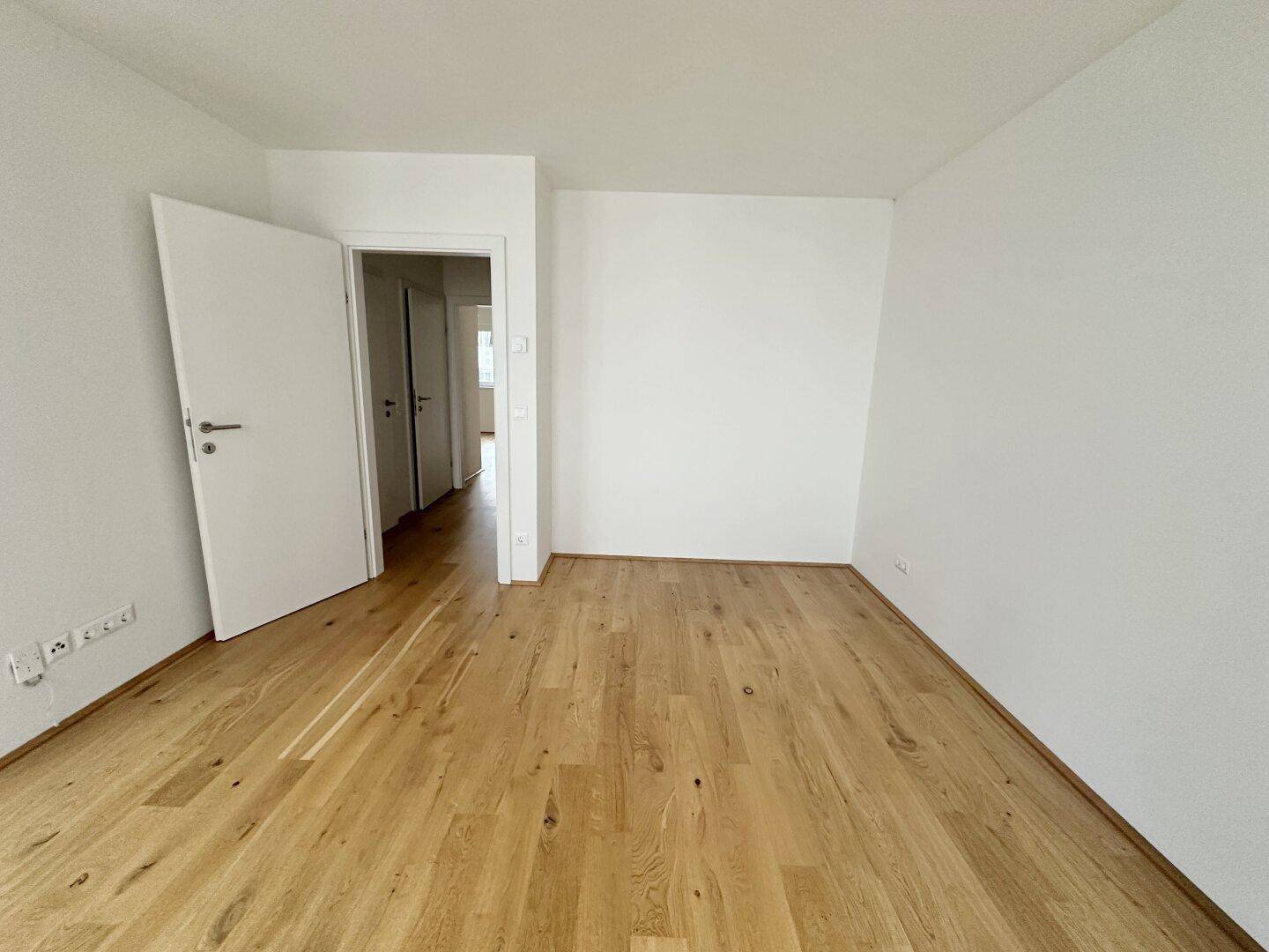 Leerer Raum mit hellem Parkettboden und mehreren Türen, die zu weiteren Zimmern führen.