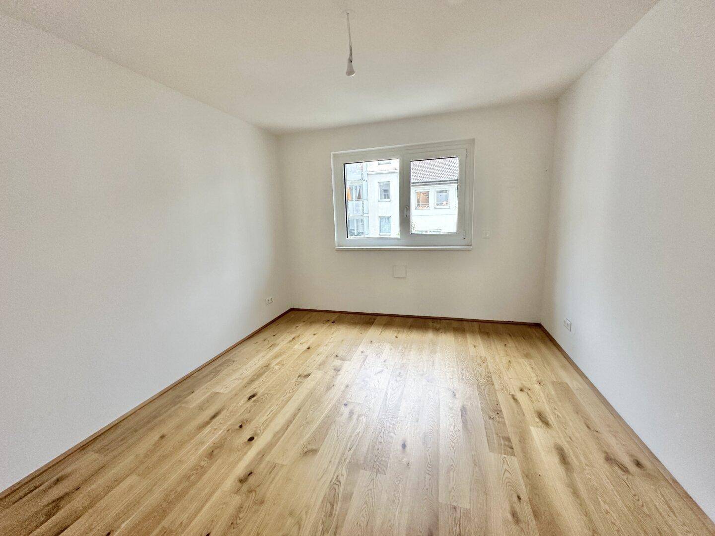 Helles Schlafzimmer mit Parkettboden und einem Fenster, das viel Tageslicht hereinlässt.