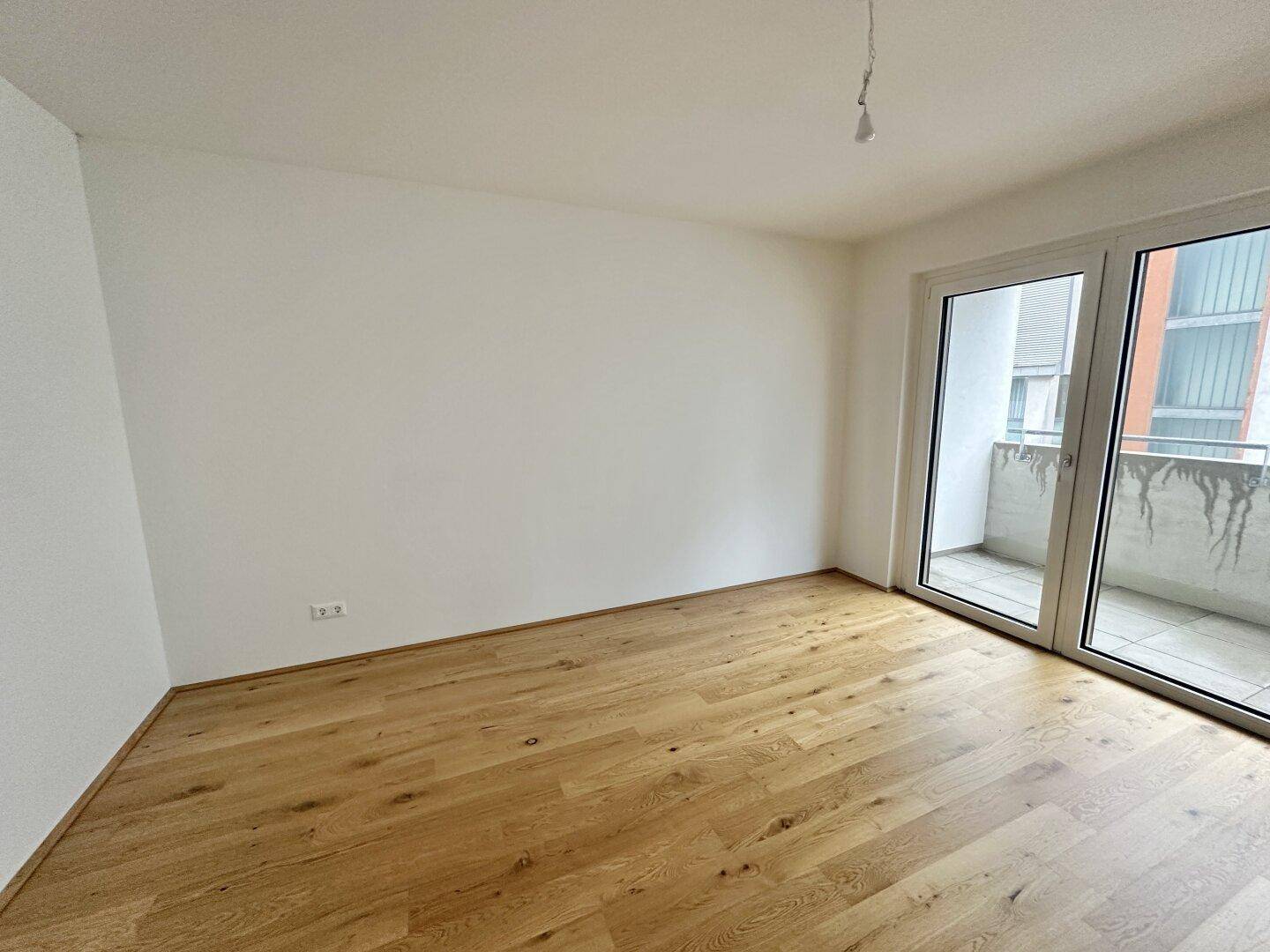 Geräumiger, leerer Raum mit neuem Parkettboden und direktem Zugang zu einem Balkon.