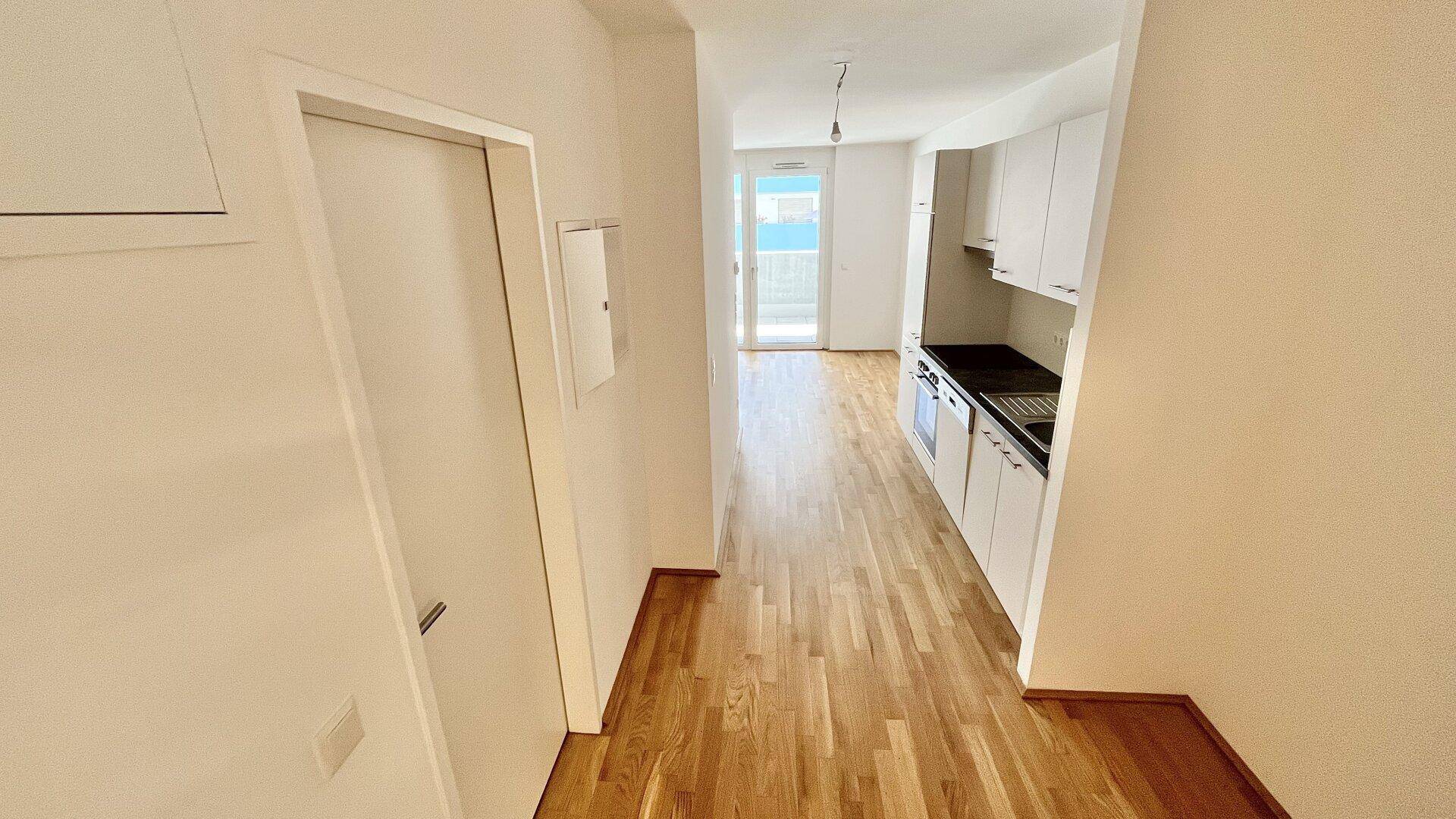 Heller Wohnbereich mit Holzboden und integrierter Küchenzeile, führt direkt zum Balkon.