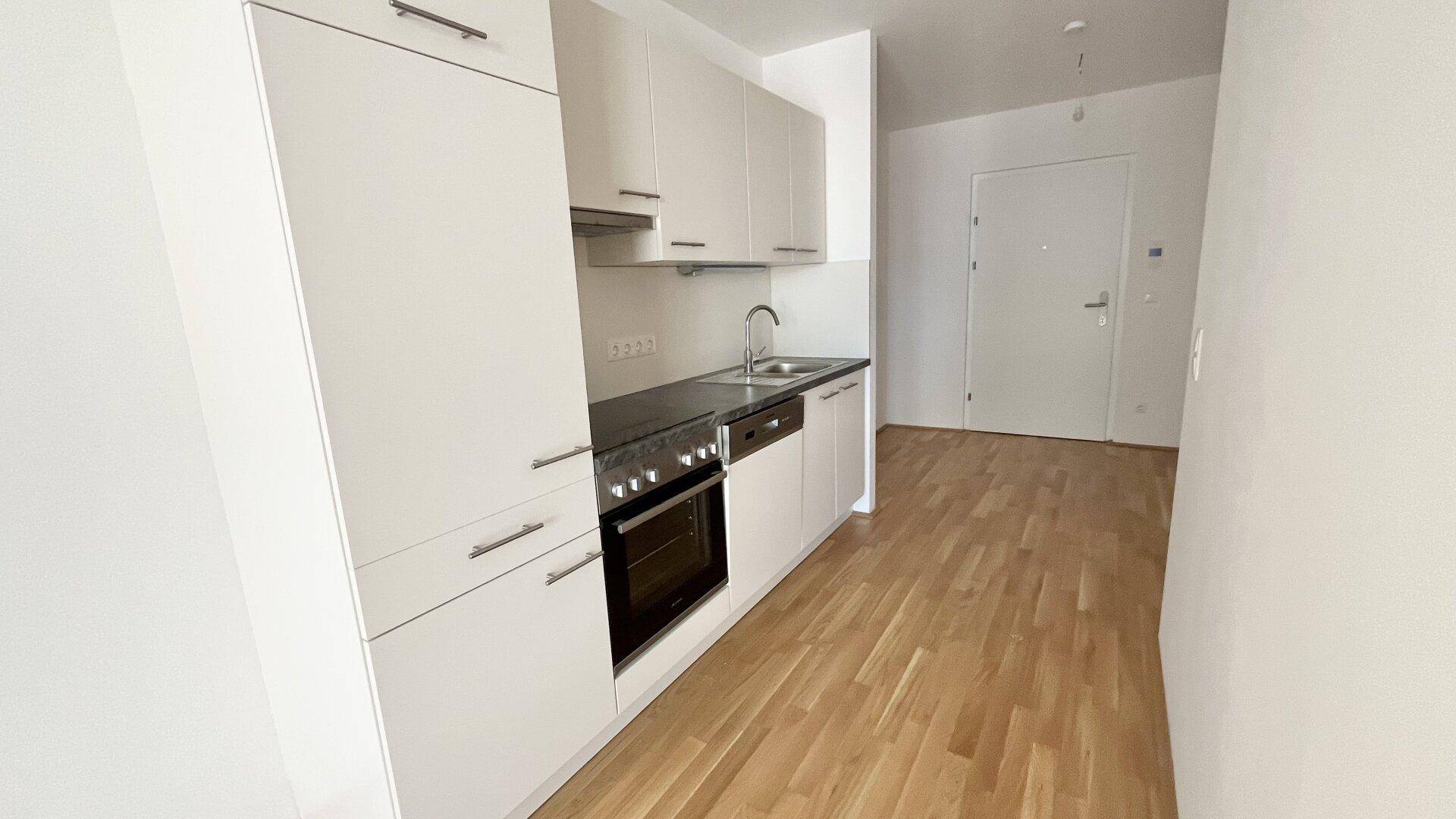 Moderne Küchenzeile mit weißen Schränken, integriertem Backofen und dunkler Arbeitsplatte.
