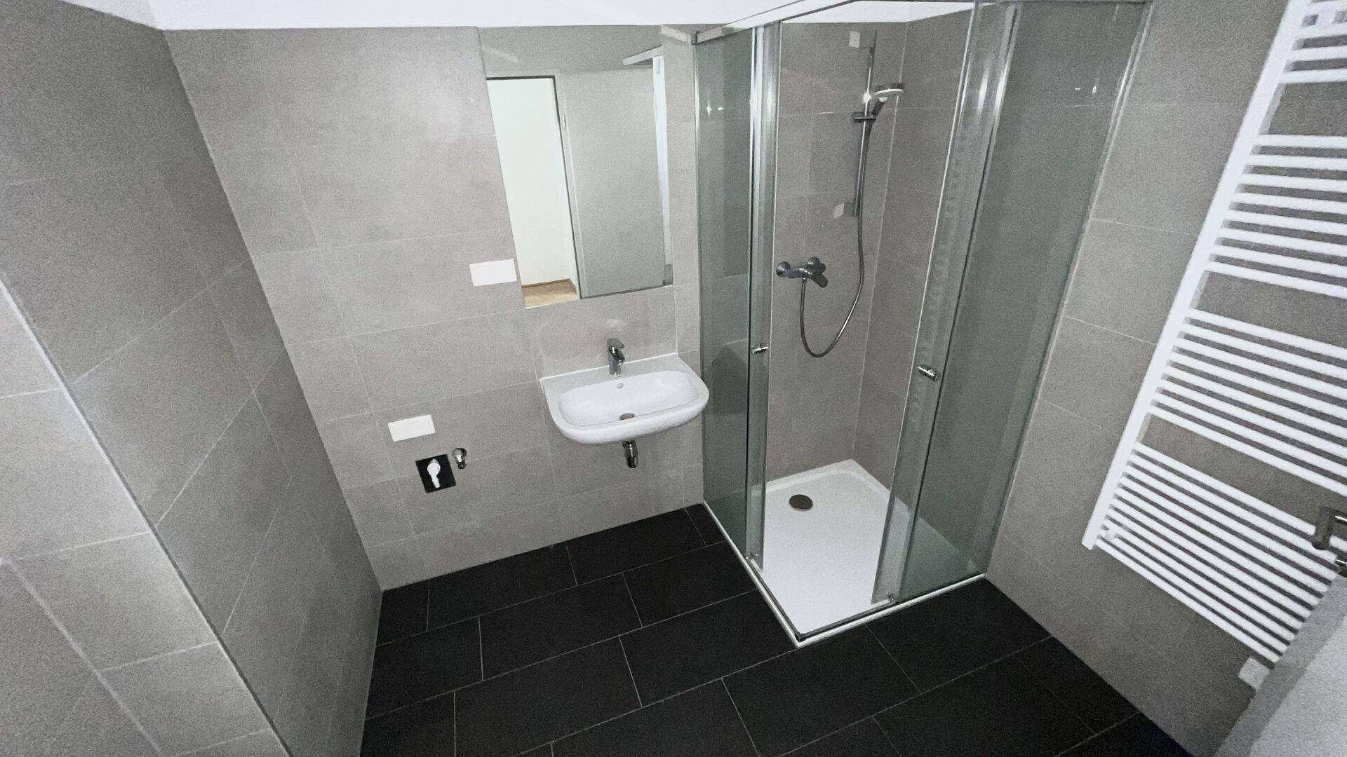 Helles Badezimmer mit Duschkabine, Einzelwaschbecken und beheiztem Handtuchhalter, modern gefliest.