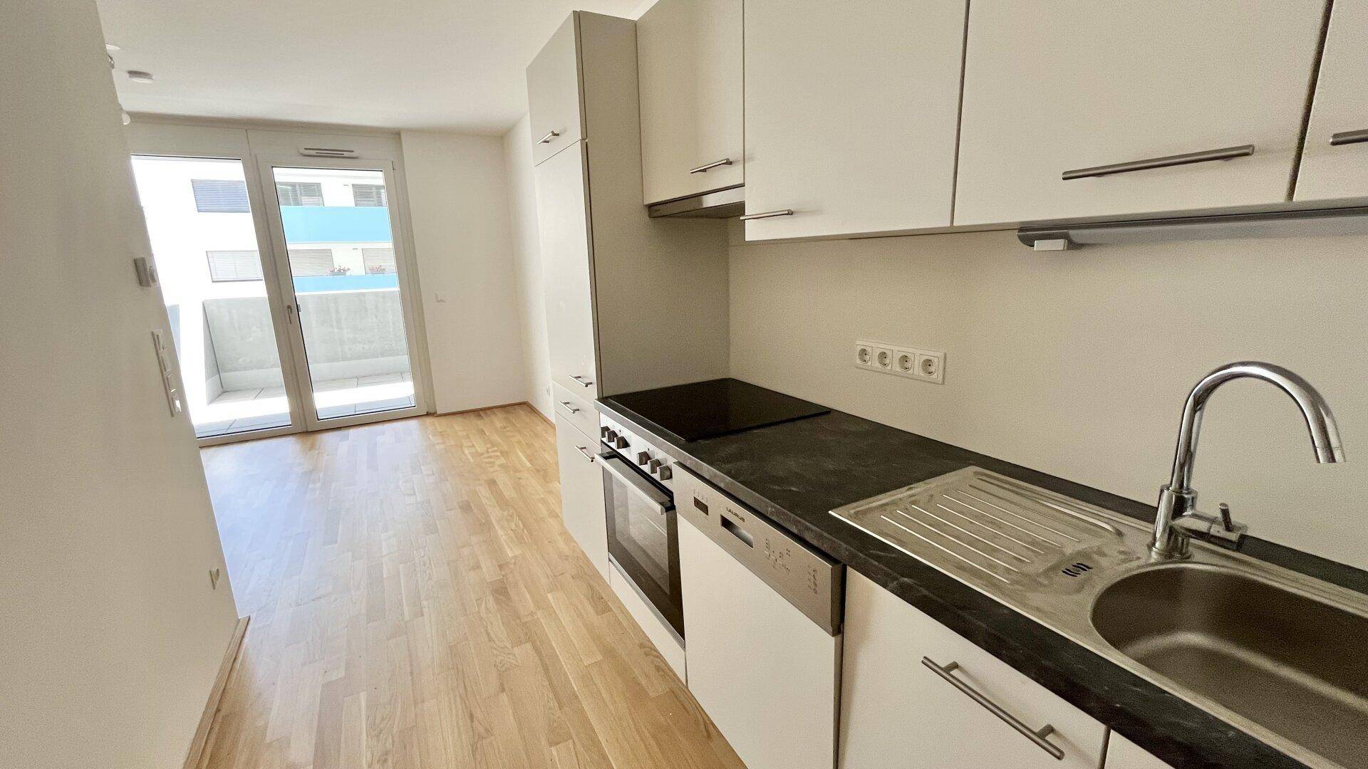 Funktionale Küchenzeile mit Spüle, Kochfeld und Backofen, mit direktem Zugang zum Balkon.