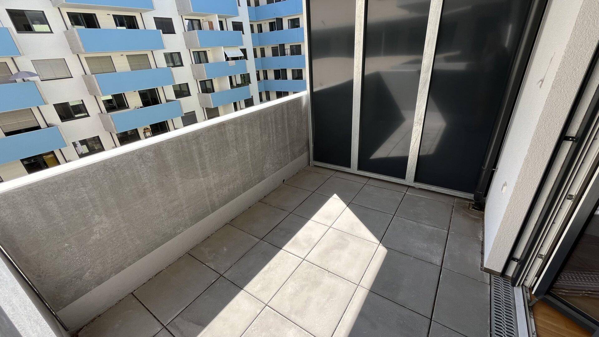 Geräumiger Balkon mit Fliesenboden und Blick auf die moderne Architektur des Nachbargebäudes.