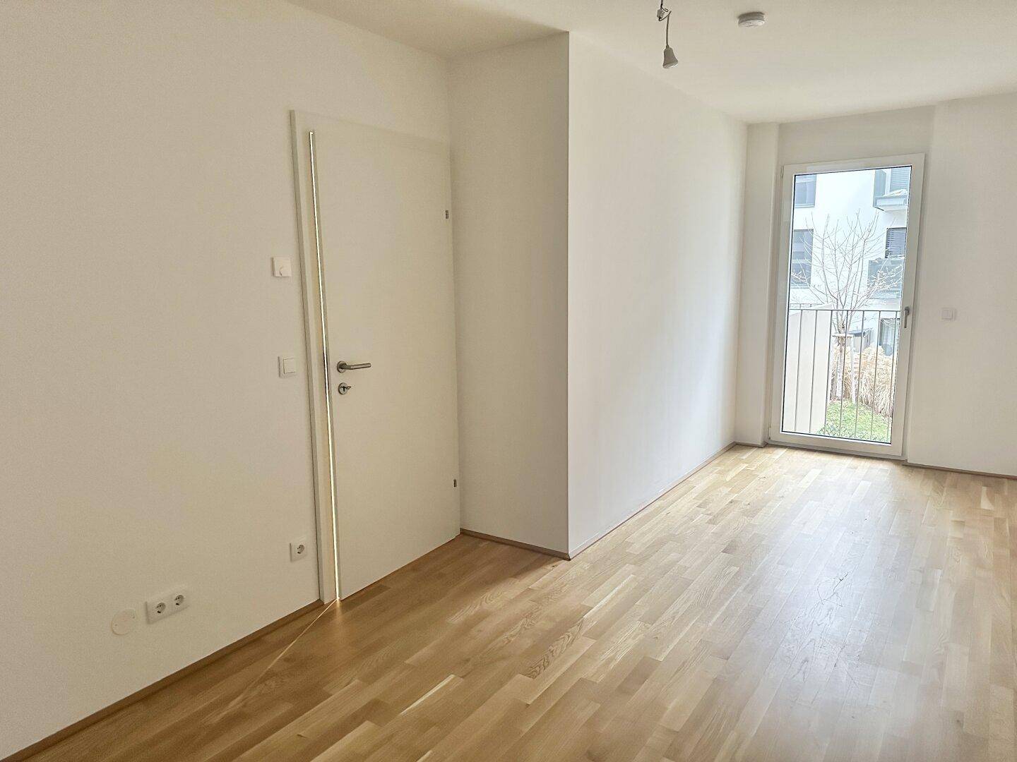 Freundliches Zimmer mit Holzboden und Zugang zu einem französischen Balkon.