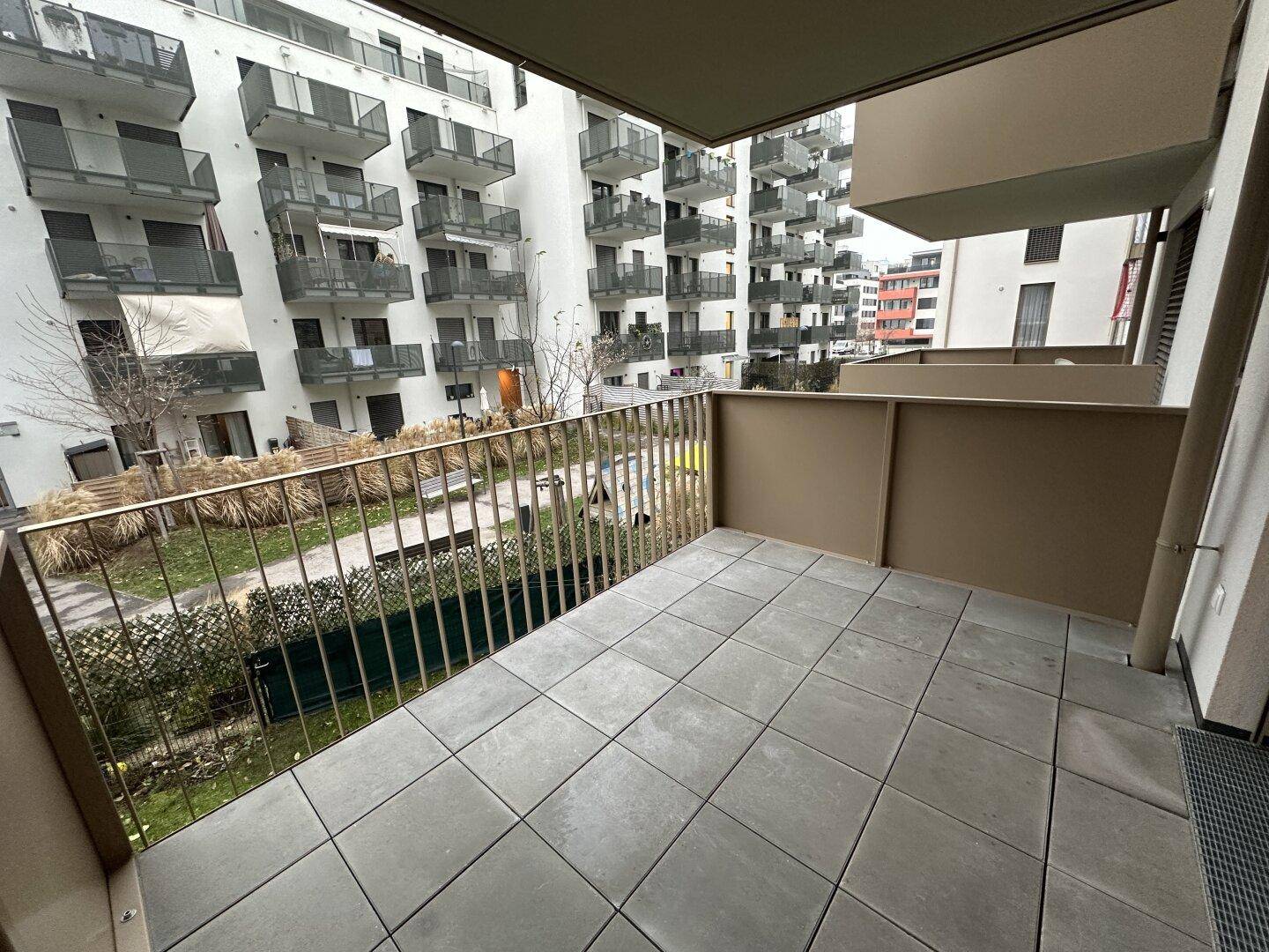 Geräumiger Balkon mit Fliesenboden und Blick auf den begrünten Innenhof der Wohnanlage.