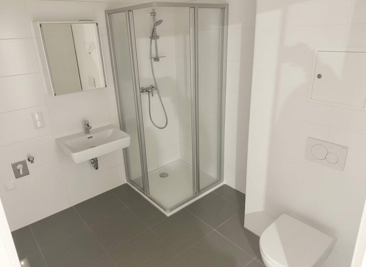 Modernes Badezimmer mit Dusche, Waschbecken und WC, ausgestattet mit hellen Fliesen.