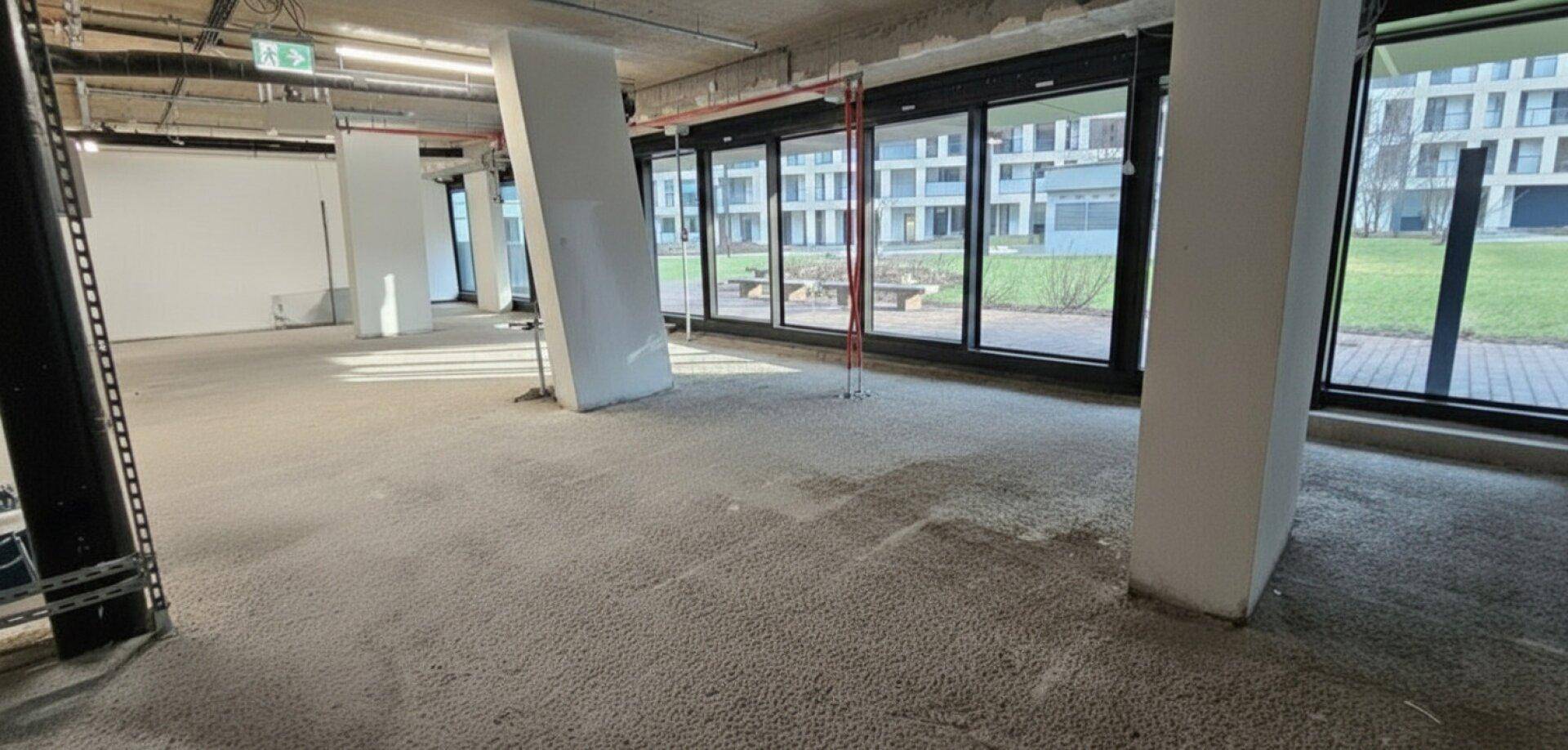 Unfertiger Bürobereich mit viel Tageslicht, Betonboden und Blick auf die umliegenden Gebäude.