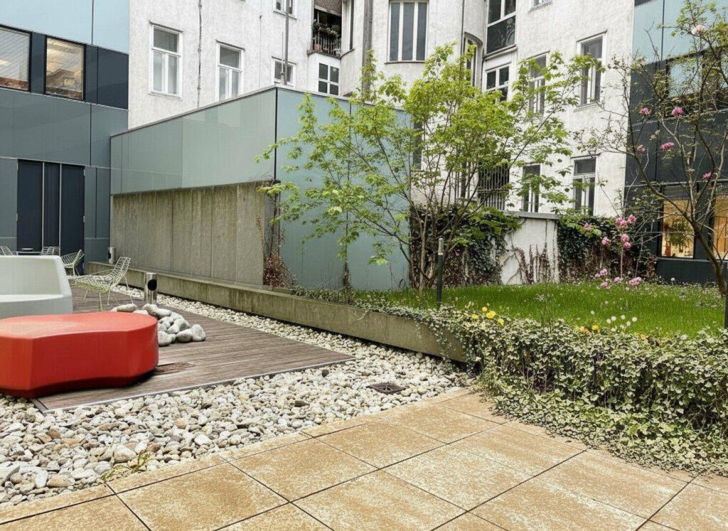 Attraktiver Innenhof mit verschiedenen Bodenbelägen, Kies, Rasenflächen und modernen Outdoor-Sitzmöbeln.