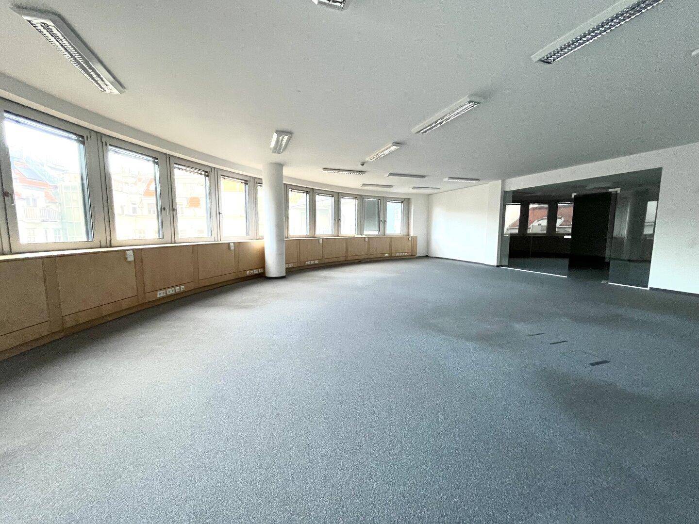 Großes, offenes Büro mit vielen Fenstern entlang einer geschwungenen Wand, ideal für Großraumbüros.