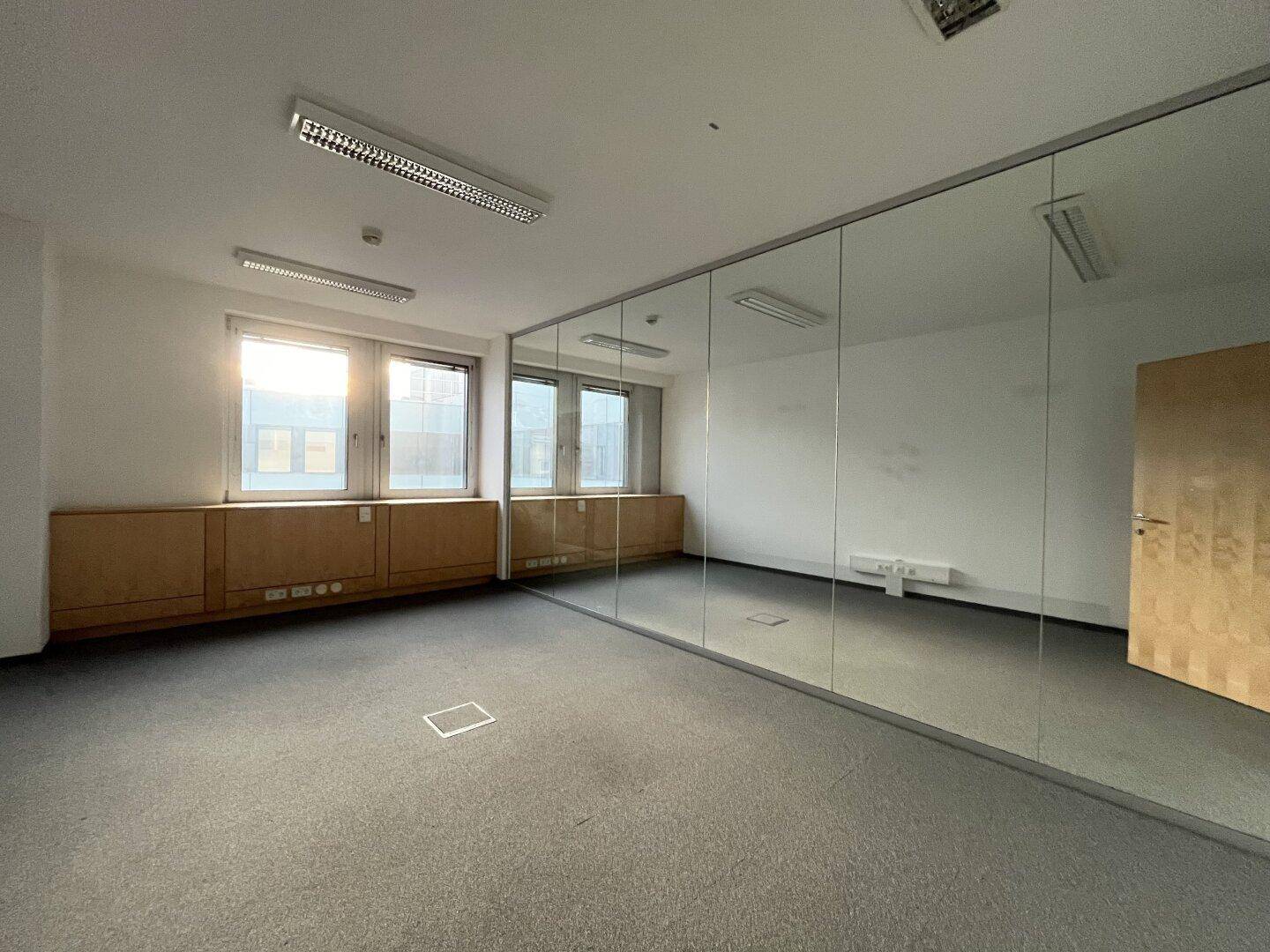 Modernes Büro mit Teppichboden und einer großen Spiegelfläche, die den Raum optisch vergrößert.