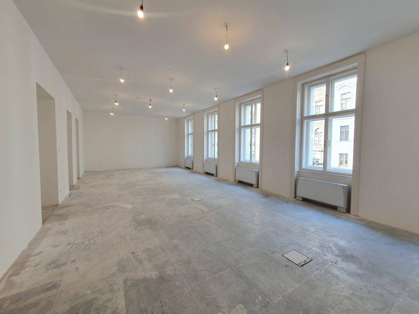 Geräumiger, heller Innenraum mit vielen Fenstern und Betonboden, ideal für Büronutzung.