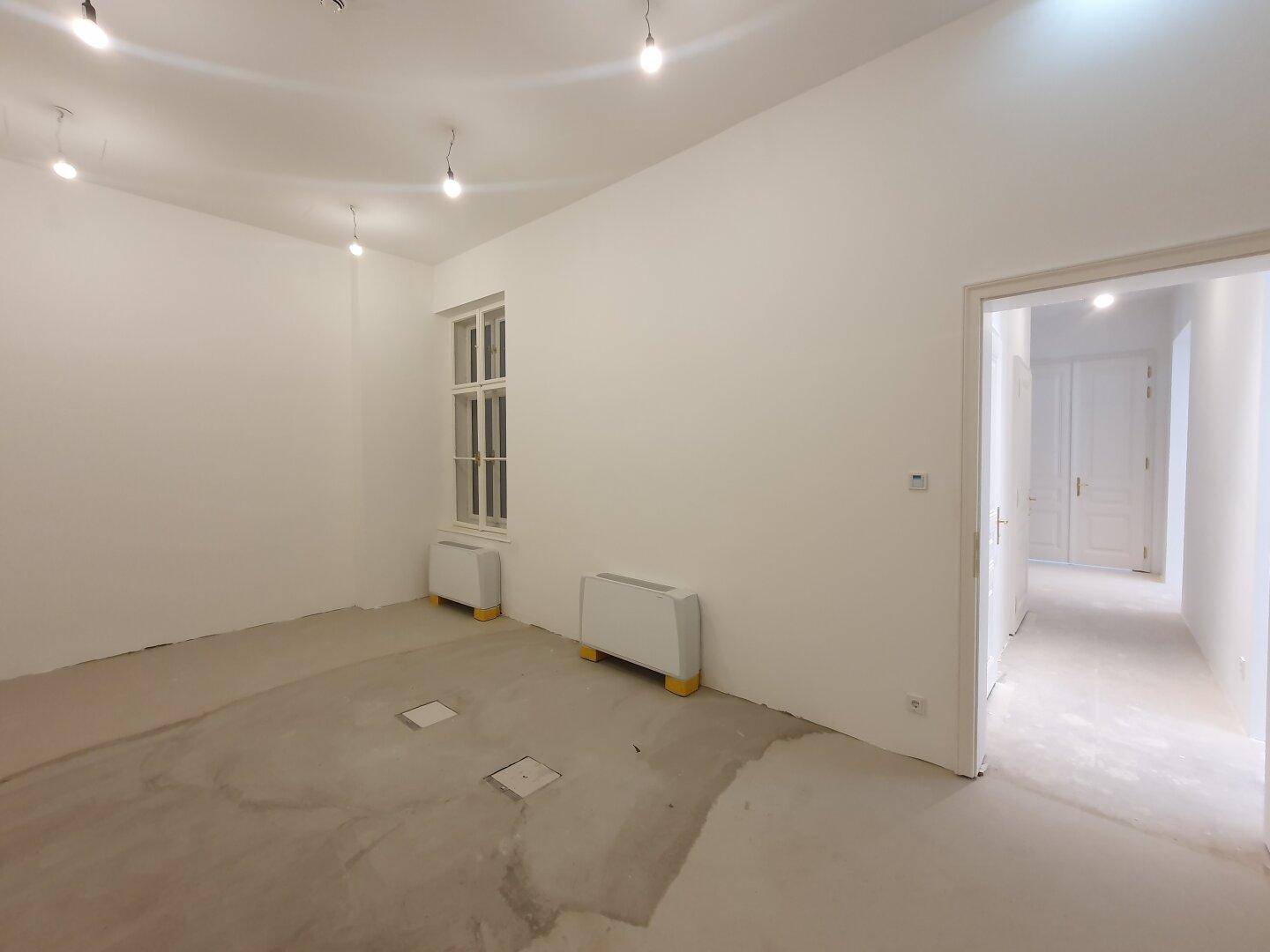 Heller Raum mit einem Fenster und Betonboden, bietet Potenzial für verschiedene Nutzungen.