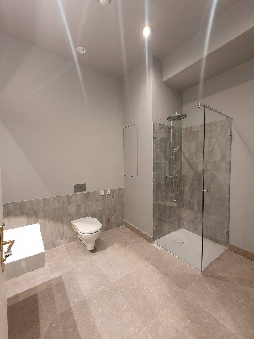 Modernes Badezimmer mit begehbarer Dusche, Wand-WC und großformatigen Fliesen.