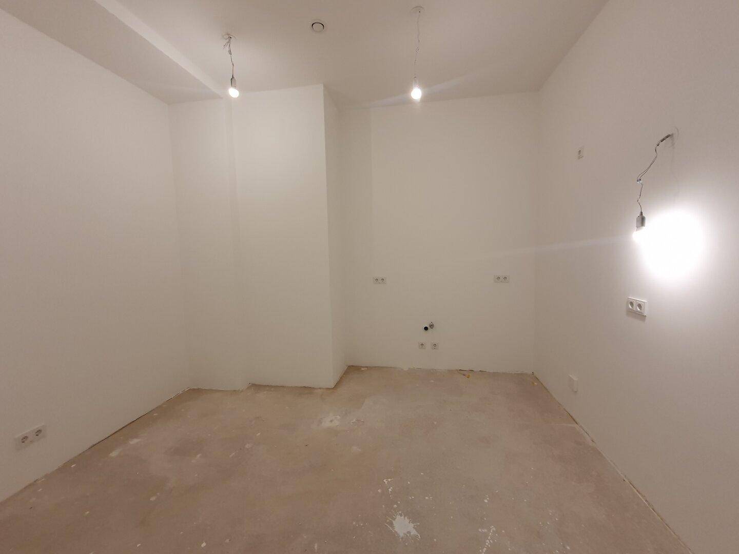 Kleiner, heller Raum mit weißen Wänden und Betonboden, ideal für ein Büro oder Abstellraum.